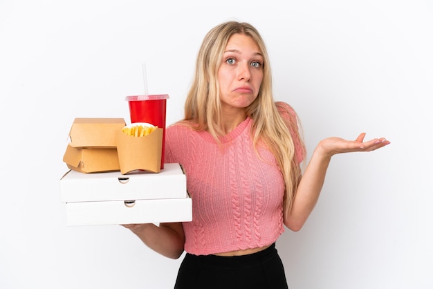 Mujer caucásica joven sosteniendo comida gorda aislada en el fondo azul que tiene dudas mientras levanta las manos