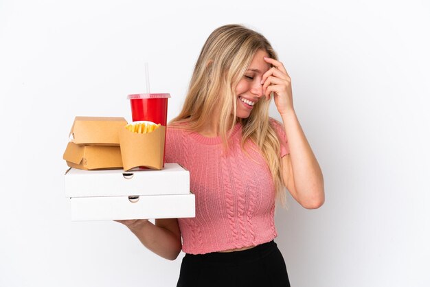 Mujer caucásica joven sosteniendo comida gorda aislada sobre fondo azul riendo