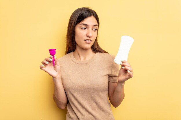 Mujer caucásica joven sosteniendo una copa menstrual aislada sobre fondo amarillo