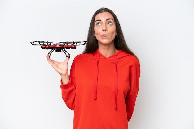 Mujer caucásica joven sosteniendo un dron aislado sobre fondo blanco y mirando hacia arriba