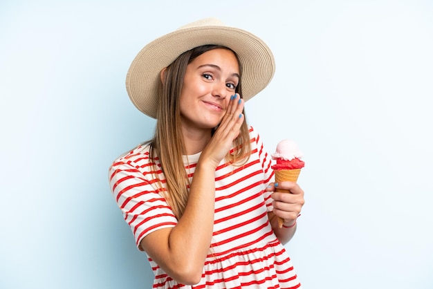 Mujer caucásica joven sosteniendo un helado aislado sobre fondo azul susurrando algo