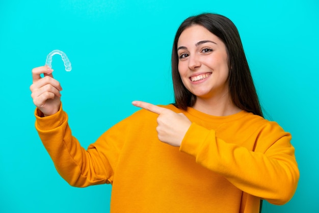 Foto mujer caucásica joven sosteniendo llaves invisibles aisladas sobre fondo azul y apuntándolo