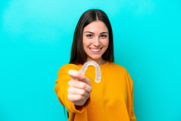 Mujer caucásica joven sosteniendo llaves invisibles aisladas sobre fondo azul con expresión feliz