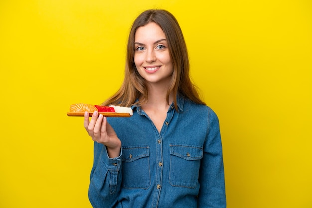 Mujer caucásica joven sosteniendo sashimi aislado sobre fondo amarillo sonriendo mucho