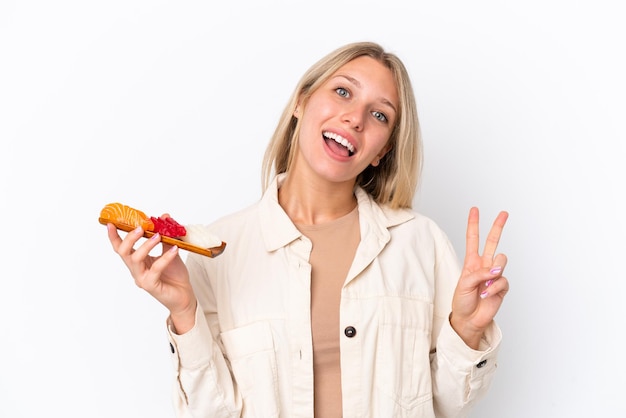 Mujer caucásica joven sosteniendo sashimi aislado sobre fondo blanco sonriendo y mostrando el signo de la victoria