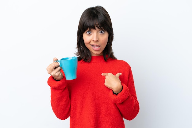 Mujer caucásica joven sosteniendo una taza de café aislada de fondo blanco con expresión facial sorpresa