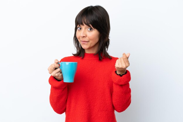 Mujer caucásica joven sosteniendo una taza de café aislado sobre fondo blanco haciendo gesto de dinero