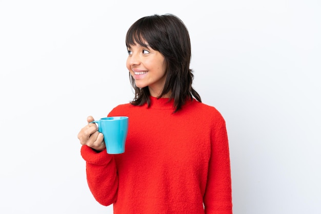 Mujer caucásica joven sosteniendo una taza de café aislado sobre fondo blanco mirando hacia el lado