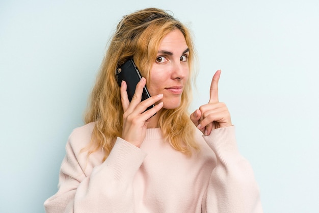 Mujer caucásica joven sosteniendo teléfono móvil aislado sobre fondo azul.