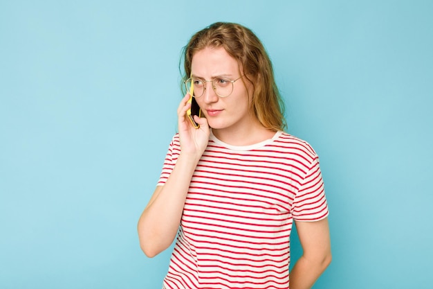 Mujer caucásica joven sosteniendo teléfono móvil aislado sobre fondo azul.