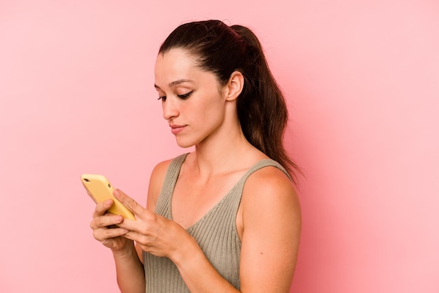 Mujer caucásica joven sosteniendo teléfono móvil aislado sobre fondo de color rosa