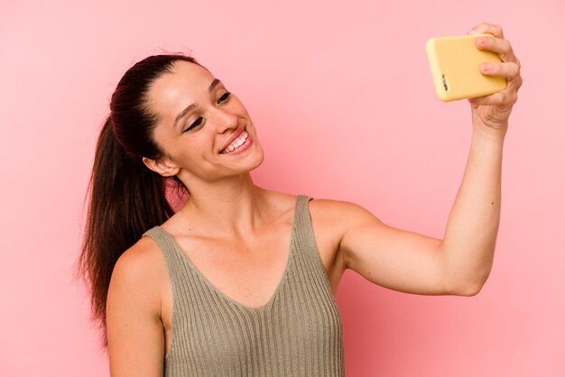 Foto mujer caucásica joven sosteniendo teléfono móvil aislado sobre fondo de color rosa