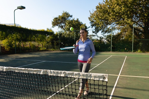 Mujer caucásica jugando tenis rebotando la pelota en la raqueta en la cancha de tenis al aire libre