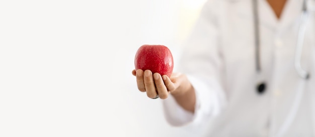 Mujer caucásica madura doctora nutricionista en bata blanca muestra manzana en el panorama interior de la oficina