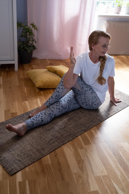 Mujer caucásica madura haciendo entrenamiento de pose de yoga retorcido en casa
