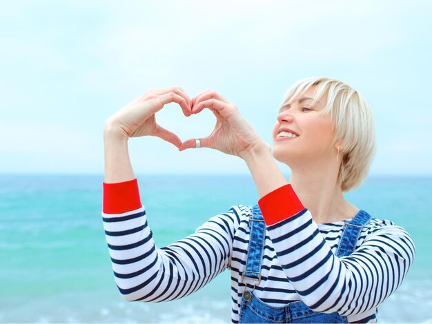 mujer caucásica con las manos como signo de amor de vacaciones junto al mar