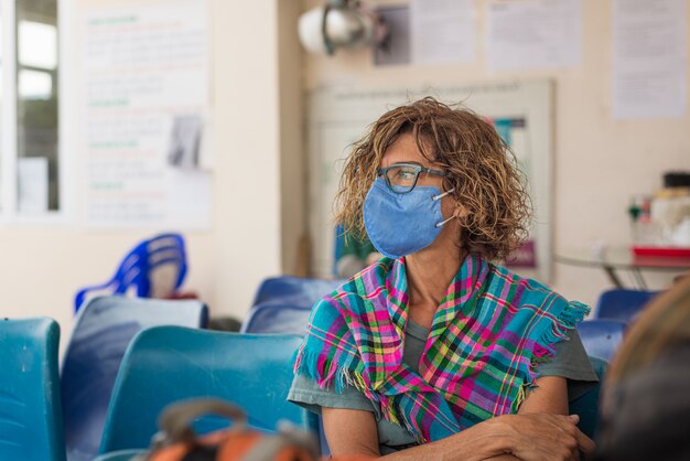 Mujer caucásica con máscara sanitaria en interiores mientras viaja en Vietnam. Turista en sala de espera con máscara médica de protección contra el riesgo del nuevo virus corona covid-19 en Asia