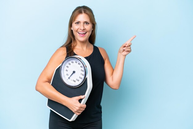 Mujer caucásica de mediana edad aislada de fondo azul con máquina de pesaje