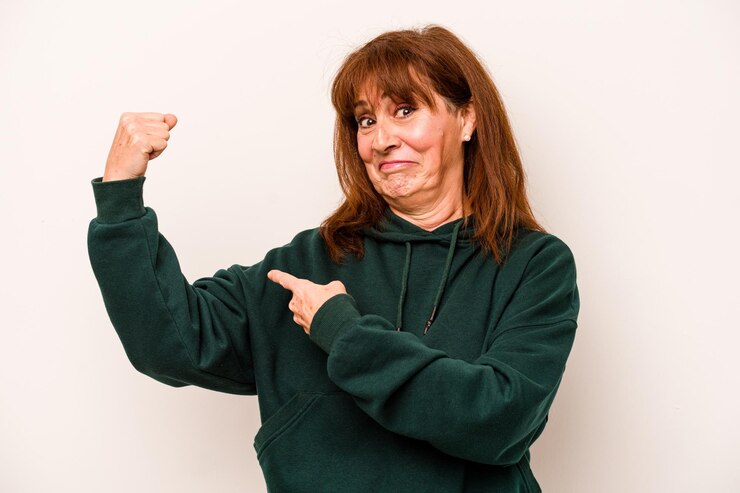 Foto mujer caucásica de mediana edad aislada de fondo blanco que muestra un gesto de fuerza con los brazos símbolo del poder femenino