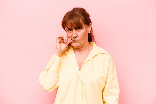 Mujer caucásica de mediana edad aislada de fondo rosa con los dedos en los labios guardando un secreto