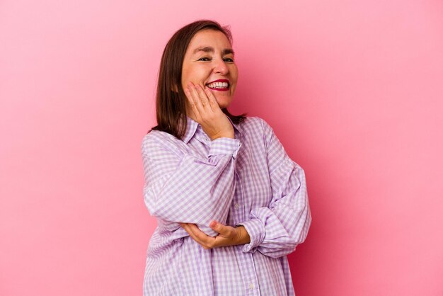 Mujer caucásica de mediana edad aislada de fondo rosa sonriendo feliz y confiada, tocando la barbilla con la mano.