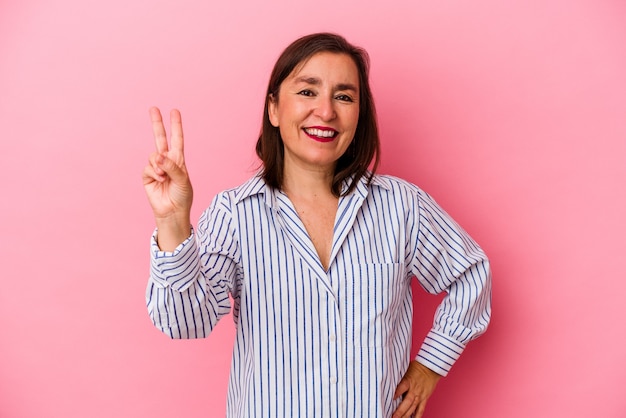 Mujer caucásica de mediana edad aislada sobre fondo rosa mostrando el número dos con los dedos.