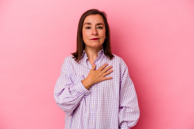 Mujer caucásica de mediana edad aislada sobre fondo rosa tomando un juramento, poniendo la mano en el pecho.