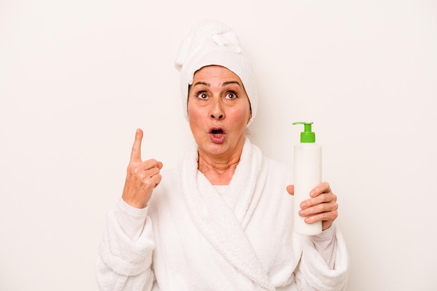 Mujer caucásica de mediana edad con un albornoz con crema corporal aislada de fondo blanco apuntando al revés con la boca abierta