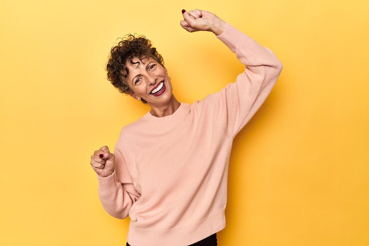 Foto mujer caucásica de mediana edad en amarillo vibrante celebrando un día especial salta y levanta los brazos con energía