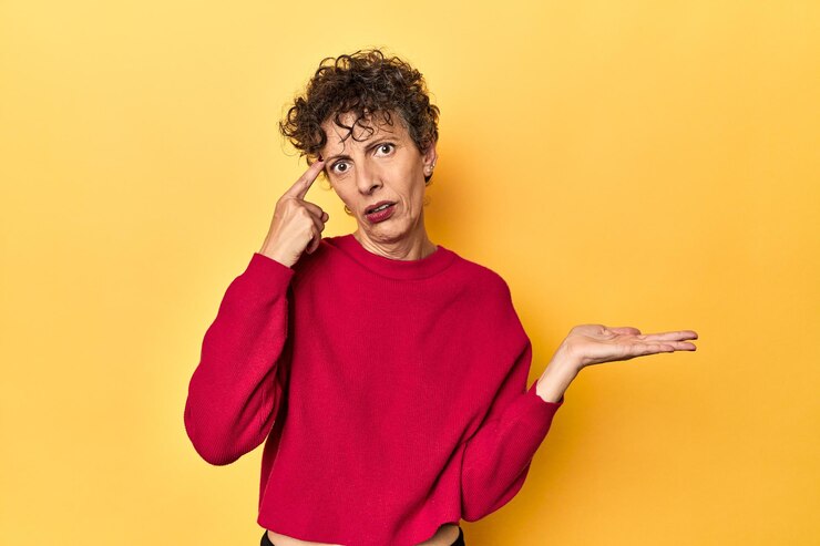 Foto mujer caucásica de mediana edad en amarillo vibrante sosteniendo y mostrando un producto en la mano