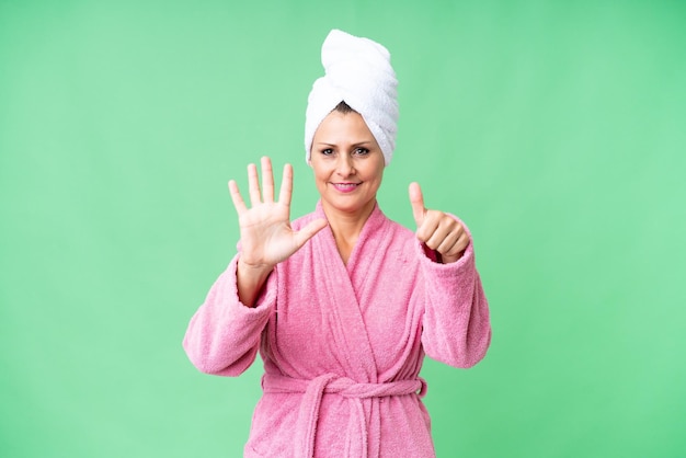 Mujer caucásica de mediana edad en una bata de baño sobre un fondo aislado contando seis con los dedos