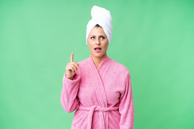 Foto mujer caucásica de mediana edad en una bata de baño sobre un fondo aislado pensando en una idea apuntando con el dedo hacia arriba