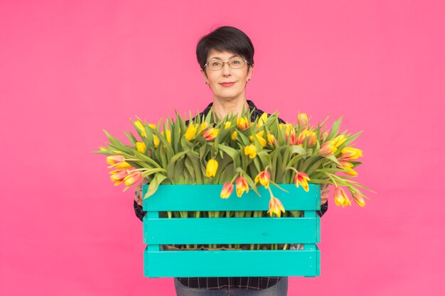 Mujer caucásica de mediana edad con caja de tulipanes en pared rosa.