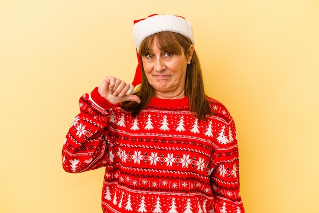 Mujer caucásica de mediana edad celebrando la Navidad aislado sobre fondo amarillo mostrando un gesto de aversión, pulgares hacia abajo. Concepto de desacuerdo.