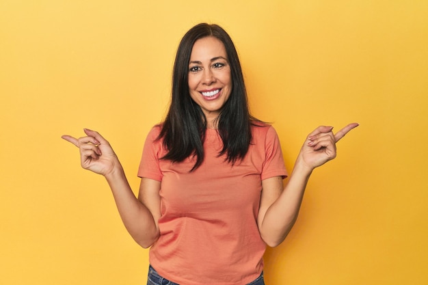 Mujer caucásica de mediana edad con un fondo amarillo apuntando a diferentes espacios de copia eligiendo uno