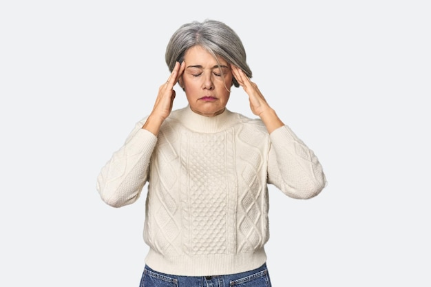 Mujer caucásica de mediana edad en el fondo del estudio tocando las sienes y teniendo dolor de cabeza