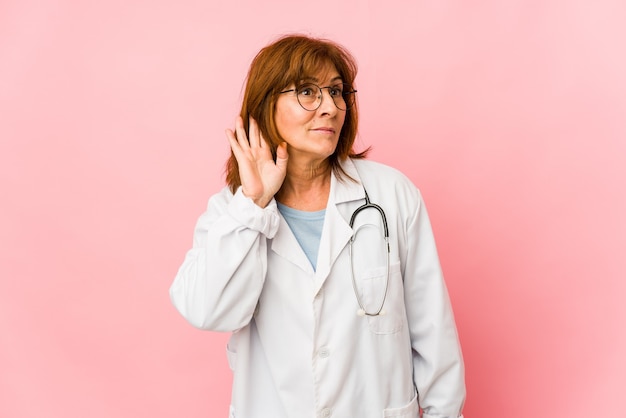 Mujer caucásica de mediana edad médico aislada tratando de escuchar un chisme.