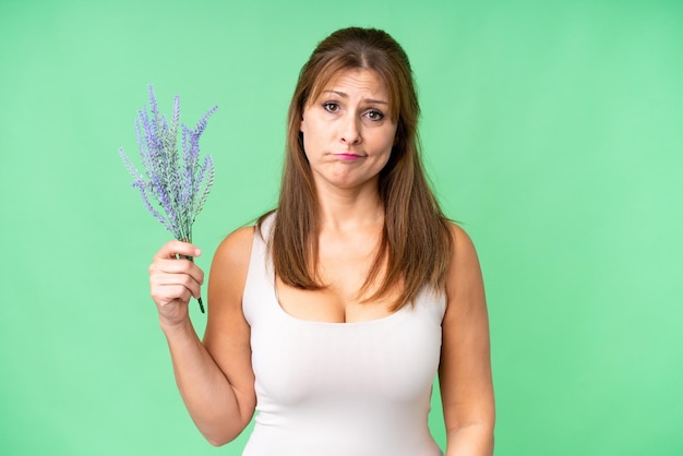 Mujer caucásica de mediana edad sosteniendo lavanda sobre un fondo aislado con expresión triste