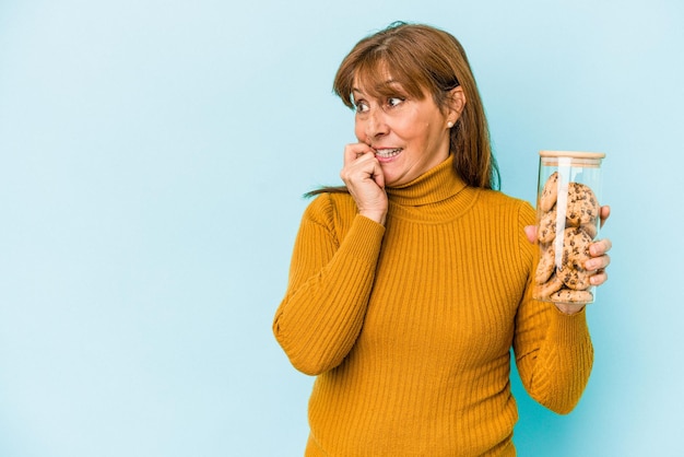 Mujer caucásica de mediana edad con tarro de galletas aislado sobre fondo azul relajado pensando en algo mirando un espacio de copia.