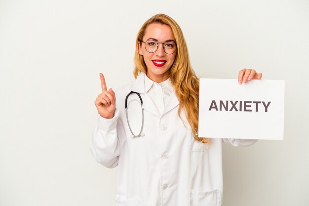 Mujer caucásica del médico que sostiene un cartel de la ansiedad aislado en el fondo blanco que muestra el número uno con el dedo.