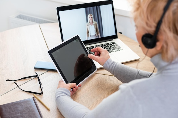 Una mujer caucásica moderna y sonriente de los años 60 con auriculares ve un seminario web en línea en casa. Feliz anciana canosa diviértete estudiando en internet. Concepto de tecnología para personas mayores.