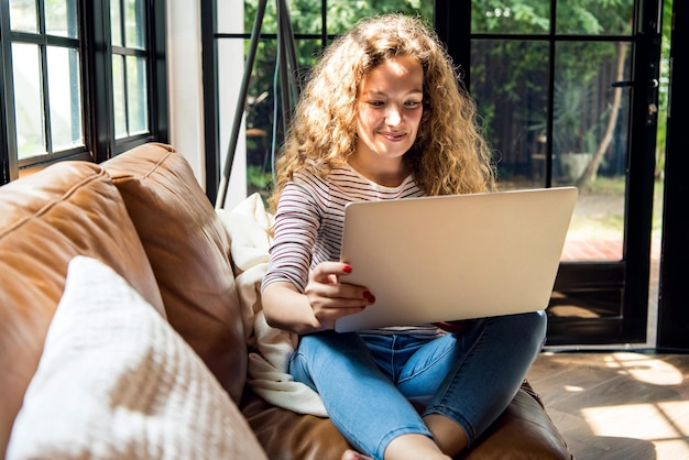 Una mujer caucásica muy sonriente que usa una computadora portátil en el sofá de casa