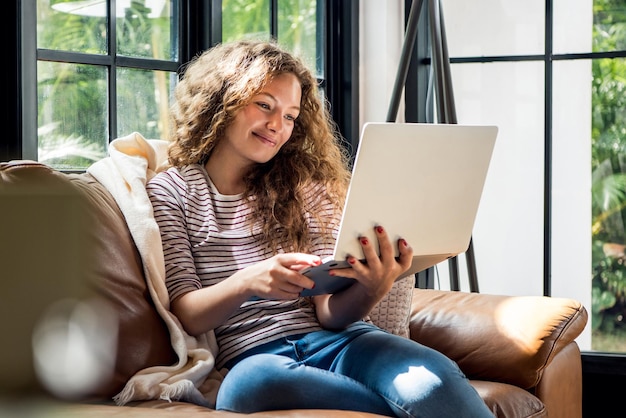 Una mujer caucásica muy sonriente que usa una computadora portátil en el sofá de casa