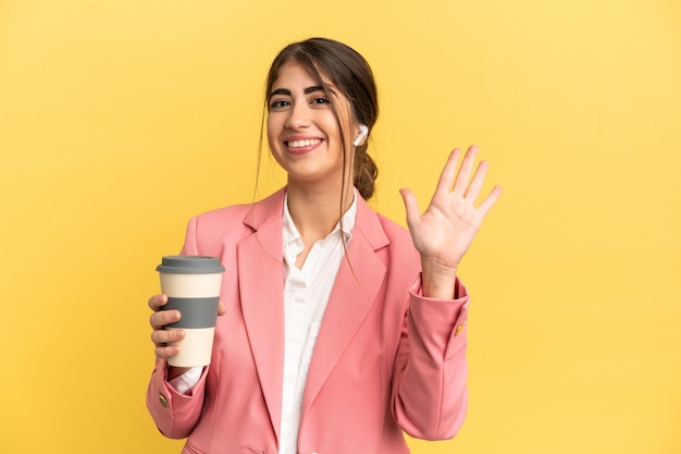 Mujer caucásica de negocios aislada sobre fondo amarillo saludando con la mano con expresión feliz