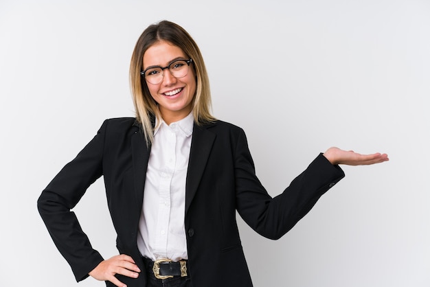 Mujer caucásica de negocios joven mostrando un espacio de copia en la palma y sosteniendo otra mano en la cintura.