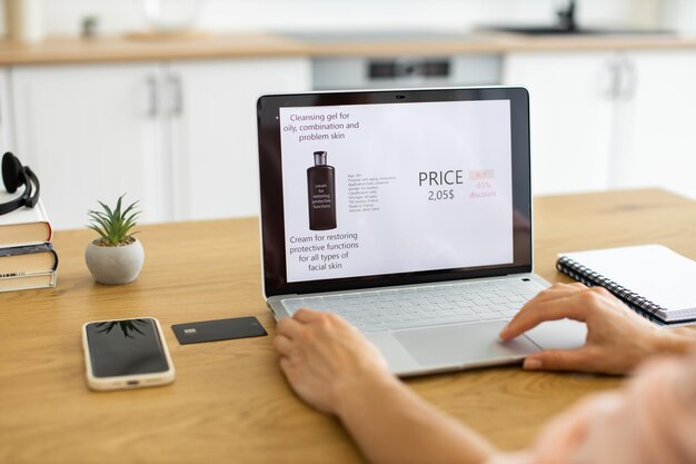 Mujer caucásica ordenando cosméticos en línea usando una computadora portátil en el escritorio de casa