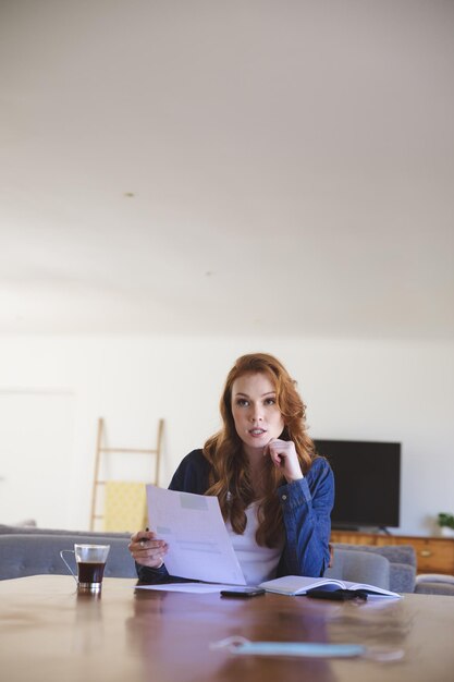 Mujer caucásica pasando tiempo en casa, en la sala de estar, trabajando desde casa, sosteniendo un trozo de papel. Distanciamiento social durante el cierre de cuarentena del coronavirus Covid 19.