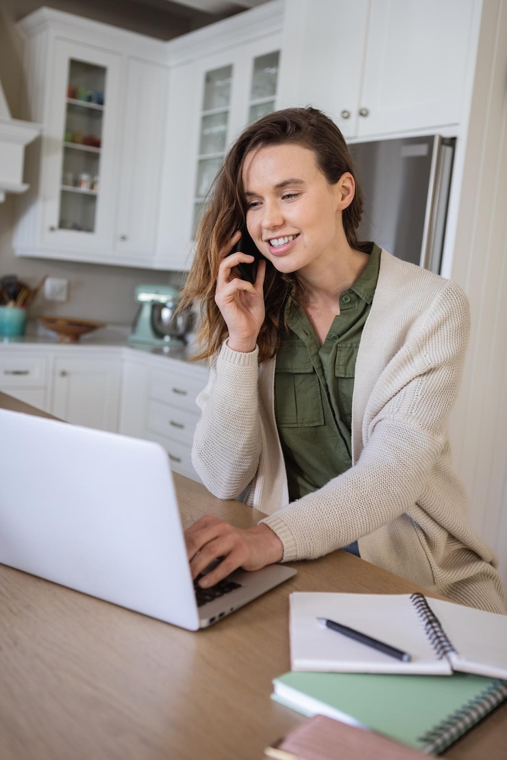 Foto mujer caucásica pasando tiempo en casa, usando su computadora portátil, trabajando desde casa, hablando por teléfono. estilo de vida en casa aislado, distanciamiento social en cuarentena durante la pandemia de coronavirus covid 19