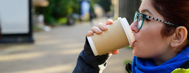 Mujer caucásica pelirroja con gafas y una chaqueta está tomando café en la calle chica disfruta de una guerra