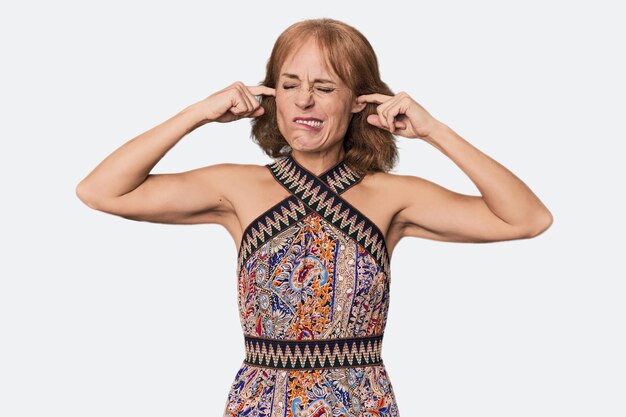 Foto mujer caucásica pelirroja de mediana edad en el estudio cubriendo las orejas con los dedos estresada y desesperada